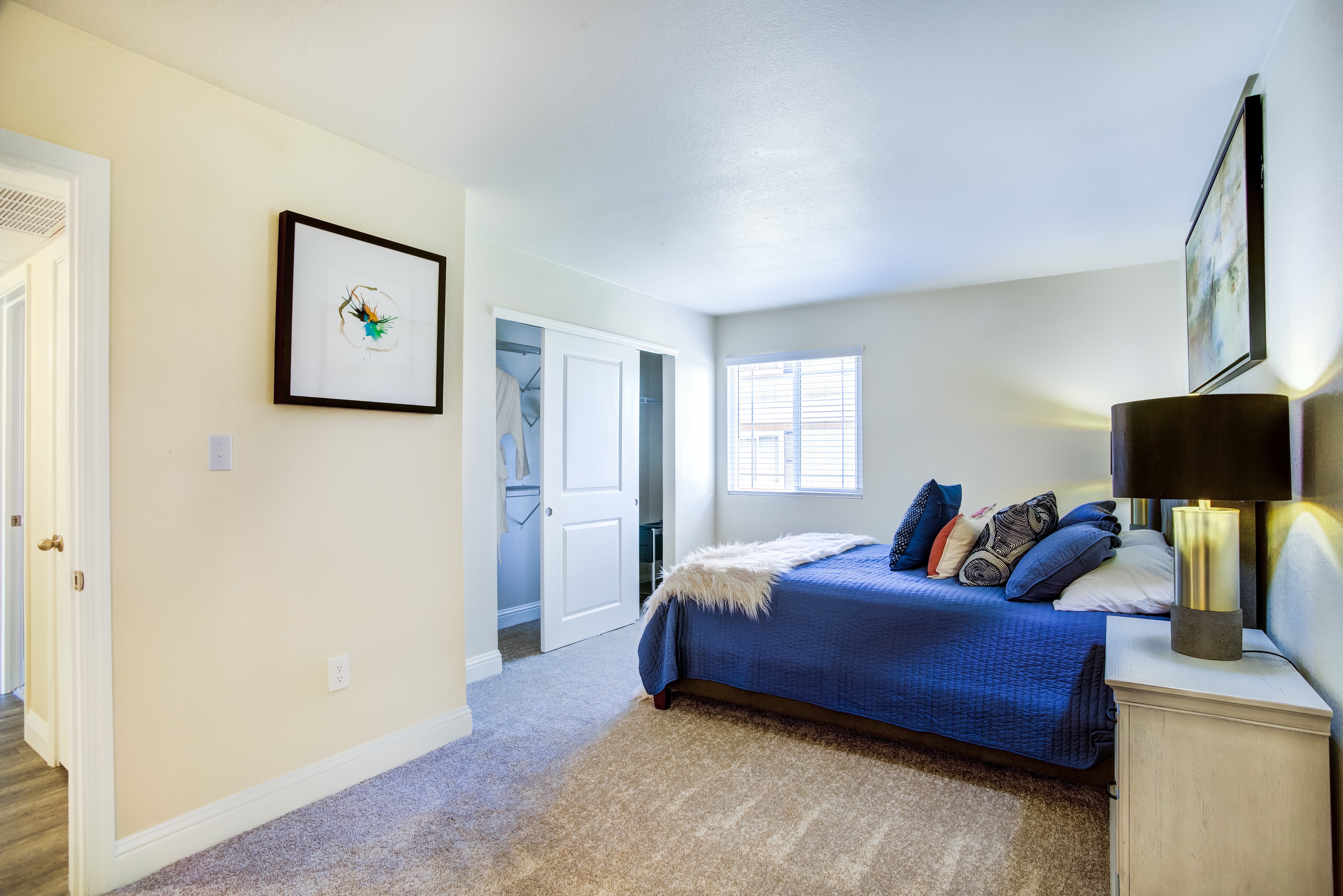 A bedroom with a blue bed and a painting on the wall.